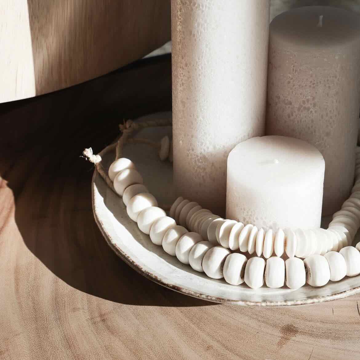 Decorative arrangement with textured pillar candles and beads on a wooden surface